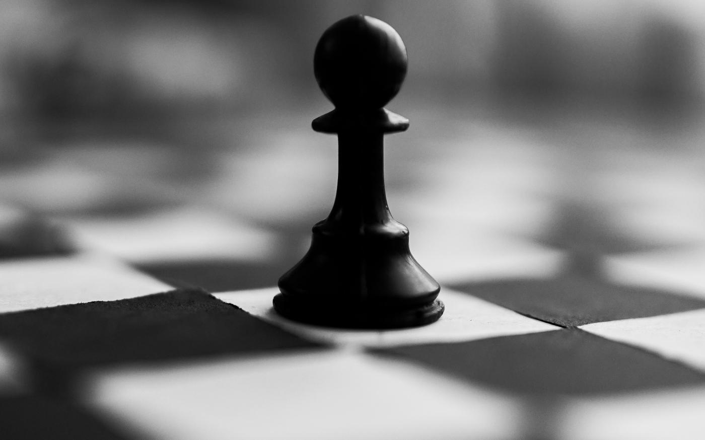 black chess piece on white and black checkered textile by Dipesh Shrestha courtesy of Unsplash.